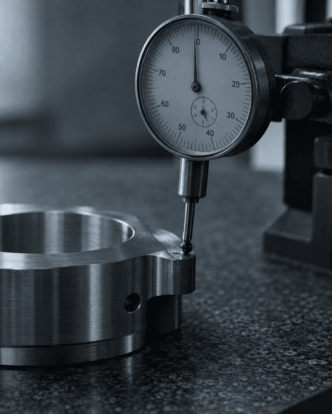 A dial indicator gauge touching a machined steel part on a granite surface plate.