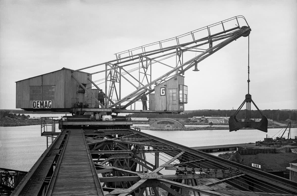 A Demag crane on its gantry at the coal port in Helsinki, 1930, its grab hanging over the water.